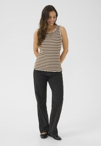 Stribet tanktop i beige og brun ribbet stof med bølgede kanter, parret med sorte straight-leg jeans og sorte flade sko.
