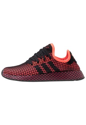 Roter und schwarzer Sportschuh mit schwarzen Schnürsenkeln und Mesh-Überzug, mit drei schwarzen Streifen und passender strukturierter Sohle.