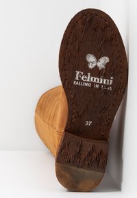 Stivale in suede marrone inclinato verso l'alto che mostra la suola di cuoio usurata con il logo a farfalla, il testo "Felmini Falling in Love" e la taglia 37 stampata.
