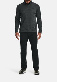 Pullover grigio scuro e texturizzato con colletto a mezza zip, abbinato a pantaloni neri e scarpe nere con dettagli verdi.