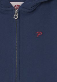 Felpa con zip blu navy realizzata in tessuto morbido, con un piccolo logo rosso sul petto e una cerniera metallica con un tirante circolare.