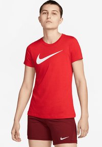Červené bavlněné tričko s kulatým výstřihem a bílým logem Nike swoosh, v kombinaci s vínovými šortkami s bílým logem. Hladká textura.