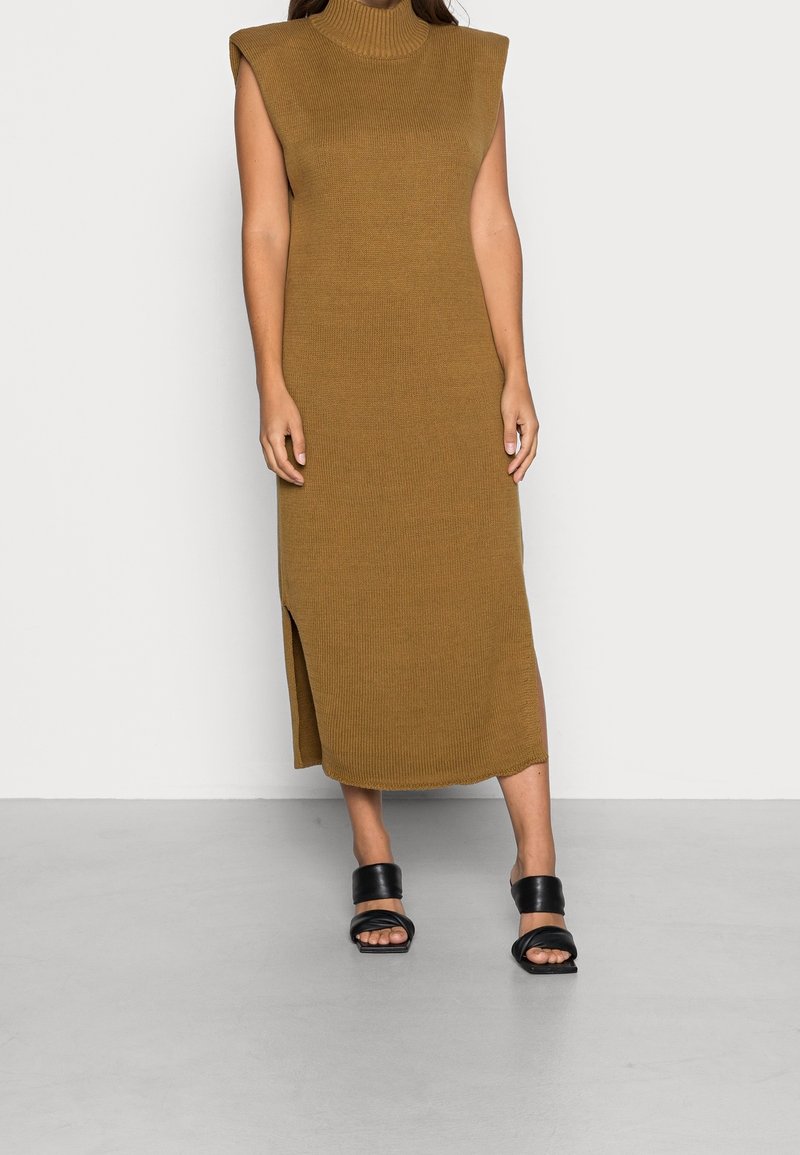 Robe en tricot côtelé vert olive à col montant et épaules découpées, avec une fente latérale, associée à des sandales noires à brides.