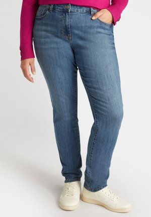 Jeans in denim blu con vestibilità slim, caratterizzati da cinque tasche, dettagli di cucitura discreti e una finitura leggermente sbiadita. Abbinate a sneakers bianche.