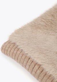 Beige faux fur tæppe med ribbede strikkede kanter. Den bløde tekstur er synlig og præsenterer en blanding af plyds- og strikkede mønstre.