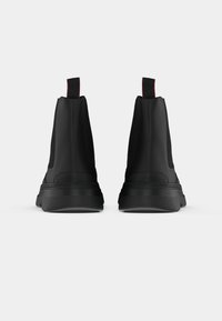 Zapatos negros de altura hasta el tobillo con una textura suave, paneles laterales elásticos y tiradores rojos en contraste en la parte posterior, que cuentan con suelas de goma resistentes.