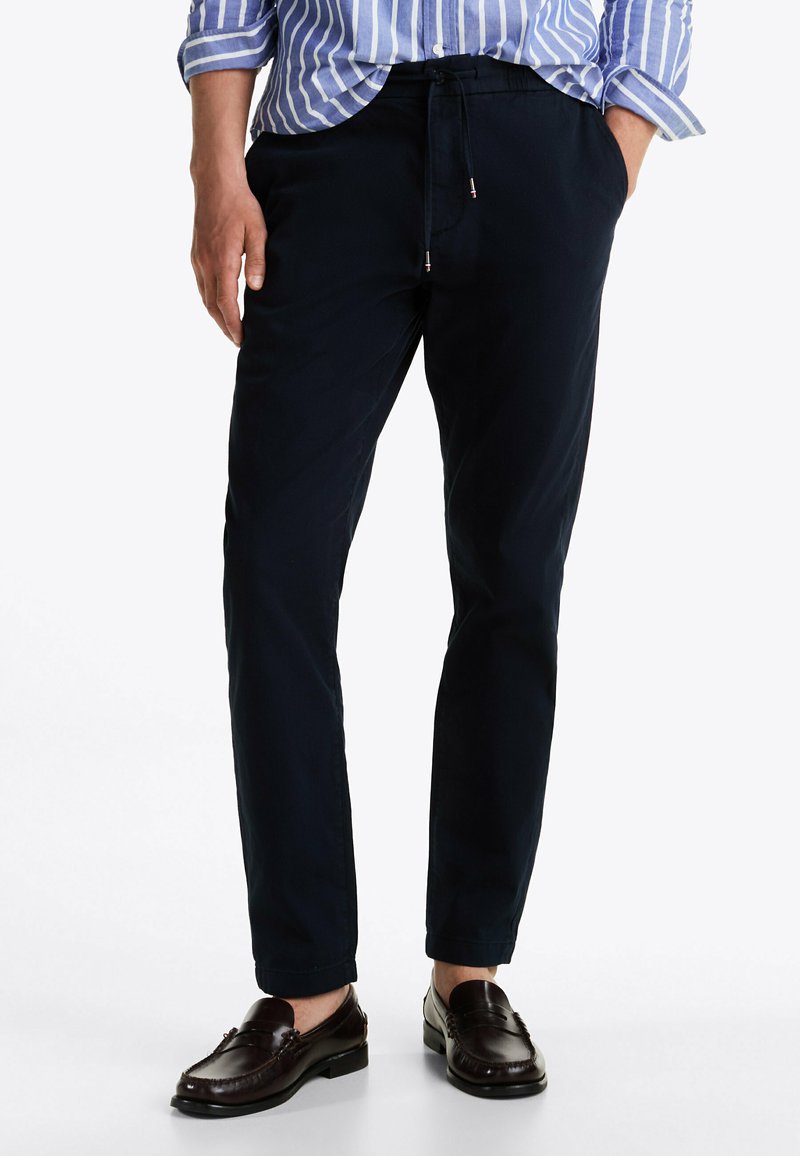 Chinos blu navy con una vestibilità rilassata, dotati di vita regolabile con cordino, tasche anteriori e texture liscia, abbinati a mocassini marroni.