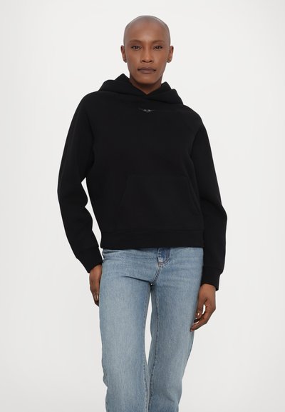 Svart hettegensere med frontlomme og cropped design. Har ribbede mansjetter og en jevn tekstur. Kombinert med lyseblå jeans.