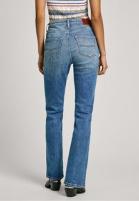 Jeans a campana blu con vita media, design a cinque tasche e dettagli di cucitura sottili, realizzati in materiale denim.