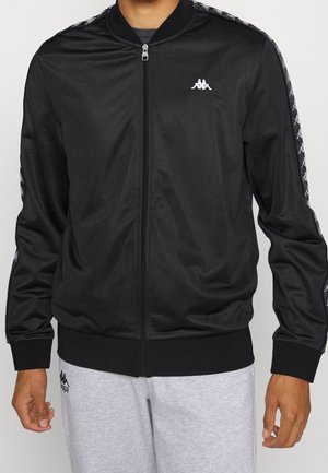 Czarna kurtka na zamek z prążkowanym kołnierzem i mankietami. Wykonana z gładkiego, błyszczącego materiału, z bocznymi kieszeniami i kontrastowymi wzorzystymi akcentami na rękawach.