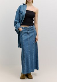Jeansrok met verticale naden, rafelige zoom, gecombineerd met een zwarte geribbelde strapless top en een losse denim jack. Bruine laarzen maken de look compleet.