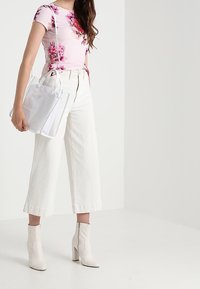 Top rosa con estampado floral, pantalones de pierna ancha blancos y botas blancas hasta el tobillo. Bolsa tote transparente con diseño estructurado. Estética simple y moderna.