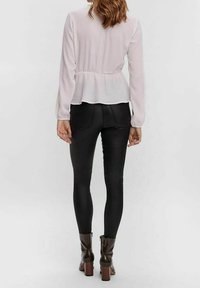 Hellrosa strukturierte Bluse mit langen Ärmeln und ausgestelltem Saum, kombiniert mit schwarzen, eng anliegenden Hosen und braunen, schmalen Ankle Boots mit Absatz.