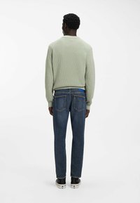 Jasnozielony, teksturowany sweter z żebrowanym wzorem, zestawiony z ciemnoniebieskimi dżinsami z dwoma tylnymi kieszeniami i niebieską metką. Czarne trampki.