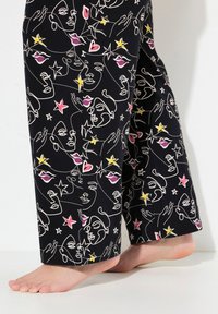 Schwarze Hose mit einem weißen Linienzeichnungsmuster, das Gesichter, Hände, Sterne und Herzen mit rosa und gelben Akzenten zeigt. Weicher Stoff, lockere Passform.