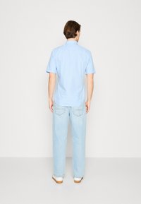 Camisa de manga corta de color azul claro con cuello puntiagudo, abotonada por la parte de atrás, combinada con jeans rectos de color azul claro y zapatillas blancas.