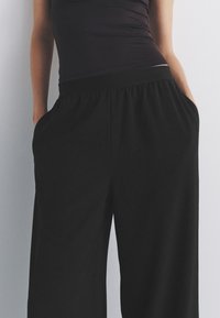 Pantalon noir à jambes larges en tissu léger, doté de poches latérales et d'une ceinture élastique pour plus de confort.
