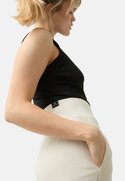 Black ribbed tank top paired with high-waisted ivory pants featuring side pockets and a visible label on the waistband.