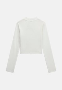 Haut blanc à manches longues, court, en tissu côtelé, avec un col montant et une silhouette ajustée. Design simple, sans motifs ni accessoires visibles.