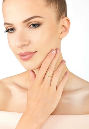 Gold ring featuring a letter "D" and a small diamond accent. Smooth surface, slim band, worn on a finger near a graceful hand. Light background.