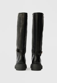 Schwarze kniehohe Stiefel aus Leder mit einer glatten Oberfläche, ausgestattet mit einem seitlichen Reißverschluss und einem Schnallenakzent an der Wade. Robuste Gummisohle.
