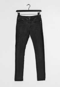 Czarne dżinsy z wąskim krojem. Posiadają pięć kieszeni, guzikowy zamek i szlufki na pasek. Tekstura pokazuje lekkie blaknięcie i zużycie.