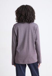 Langermet, lilla stripete topp laget av mykt stoff med løs passform, kombinert med marineblå bukser. Sett fra baksiden.
