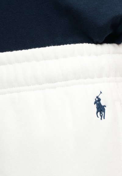 Κοντινό πλάνο λευκής ελαστικής μέσης με λογότυπο παίκτη πόλο σε μπλε ναυτικό χρώμα πάνω σε διπλωμένο ύφασμα λευκό και μπλε ναυτικό.