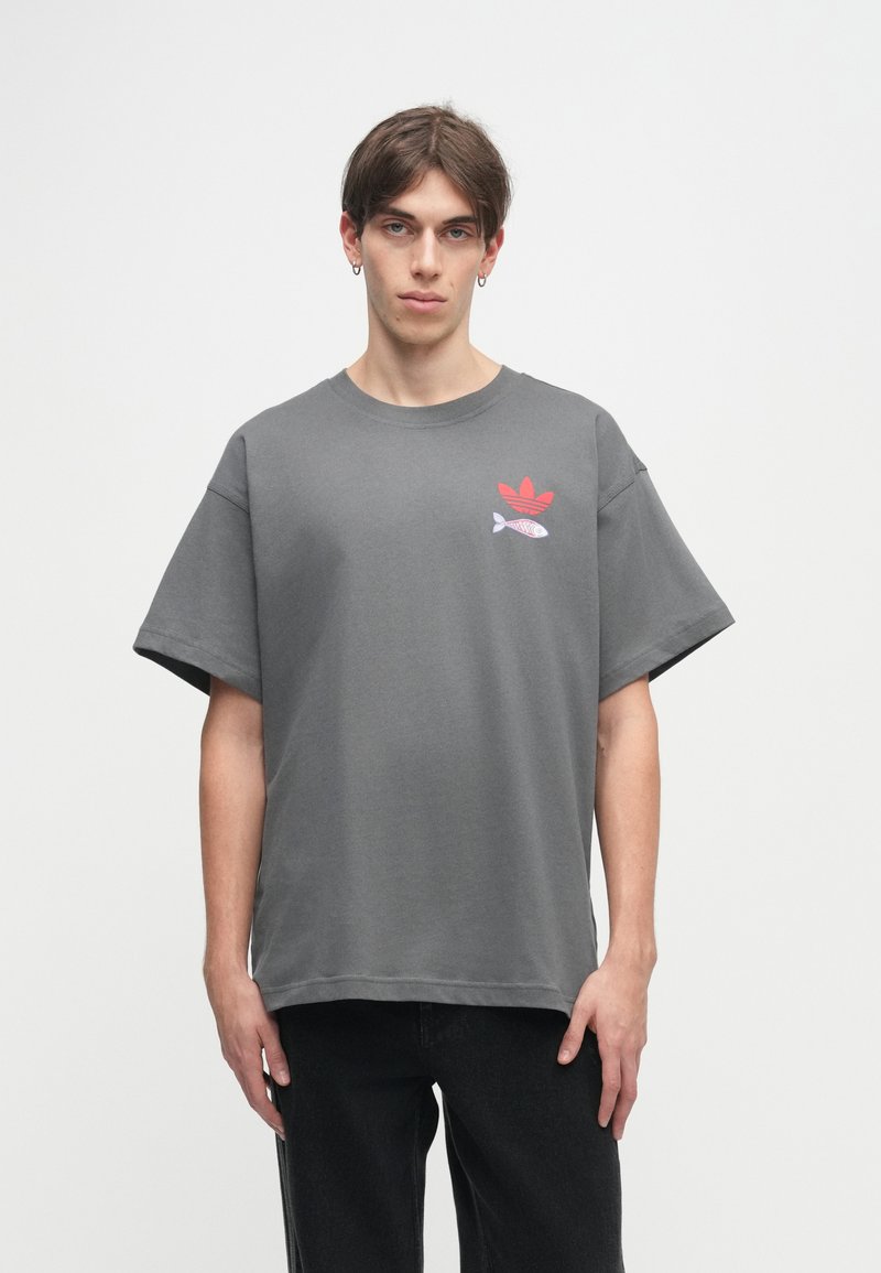 Camiseta gris de manga corta hecha de algodón, con un logo rojo y un gráfico de pez en el lado izquierdo, con un ajuste relajado y cuadrado.