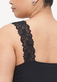 Schwarzes Spaghettiträger-Top mit einem Spitzenriemen und floralen Mustern, das eine glatte Stoffstruktur und eine figurbetonte Silhouette auf der Schulter einer Person präsentiert.