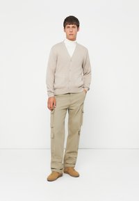 Beige ribbestrikket cardigan med v-hals og knappelukking, parret med lyse khaki cargo-bukser med sidelommer og brune sneakers.
