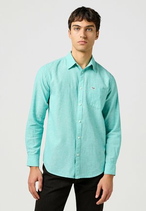 Camicia lunga a maniche raglan color turchese chiaro con chiusura a bottoni, colletto e taschino sul petto. Realizzata in un tessuto texturizzato. Presenta un piccolo logo.