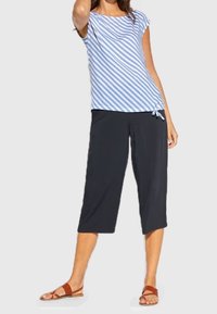 Blå och vit randig kortärmad topp med knutdetalj, matchad med svarta cropped byxor och bruna platta sandaler. Slät tyg, avslappnad passform.