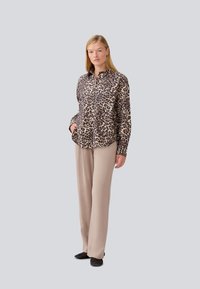 Camicia con stampa leopardata in tessuto leggero, con colletto, maniche lunghe e chiusura a bottoni. Abbinata a pantaloni beige sartoriali.