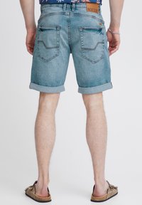 Shorts en denim bleu clair avec des ourlets retroussés, dotés de deux poches arrière et de coutures contrastantes. Portés avec des sandales marron.