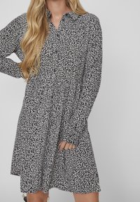 Abito floreale in bianco e nero con maniche lunghe, colletto con bottoni e gonna a ruota, realizzato in tessuto leggero.