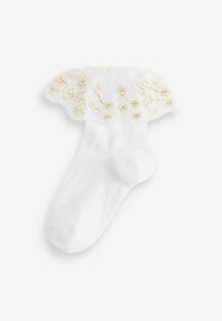 Chaussettes blanches avec un bord en dentelle froncée, ornées d'un motif floral brodé en doré, texture douce et finition lisse.