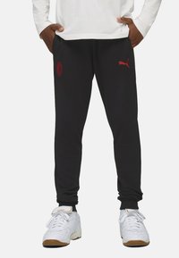 Schwarze Sweatpants mit roten gestickten Logos, elastischen Bündchen und Seitentaschen. Kombiniert mit weißen Sneakers mit einer Gummisohle.