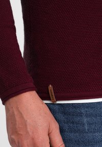 Maroon pullover sweater in a textured knit with long sleeves. Features a ribbed cuff and a small fabric tag with "ombre" at the hem.