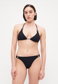Black bikini with a textured surface. Top has triangular cups with ties, and the bottom features circular accents on the sides.