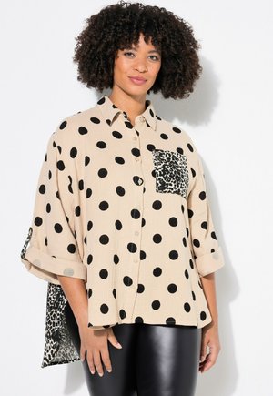 Chemise beige avec de grands pois noirs, design à boutons, manches retroussées et poche en imprimé léopard. Tissu texturé, coupe décontractée.