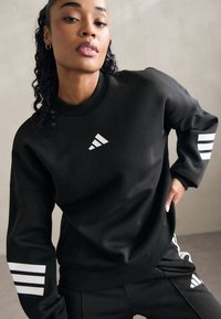 Sweatshirt noir à col rond, avec un logo blanc et trois bandes sur les manches. Fabriqué dans un tissu lisse et avec une coupe décontractée.