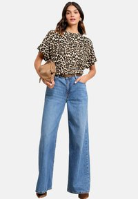 Top corto a maniche corte con stampa leopardata, vestibilità rilassata; abbinato a jeans a vita alta azzurri e larghi; la modella tiene in mano una borsa color cammello.