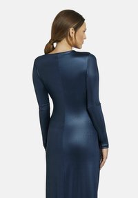 Langärmeliges Kleid in Marineblau, mit einem eleganten, glänzenden Stoff. Das Design ist figurbetont mit einem subtilen Glanz und nahtlosem Rücken.