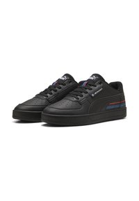 Adidași din piele neagră cu o textură netedă, cu detalii perforate, șireturi plate și dungi colorate pe lateral. Talpă din cauciuc.