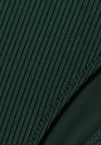 Tissu côtelé vert foncé présentant des rayures verticales, texture lisse, et un ourlet cousu avec un fil fin, mettant en avant son artisanat détaillé.