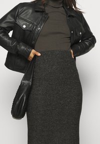 Blouson en cuir noir court sur un col roulé ajusté olive, associé à une jupe crayon texturée gris foncé ; présente un sac à main tressé noir.