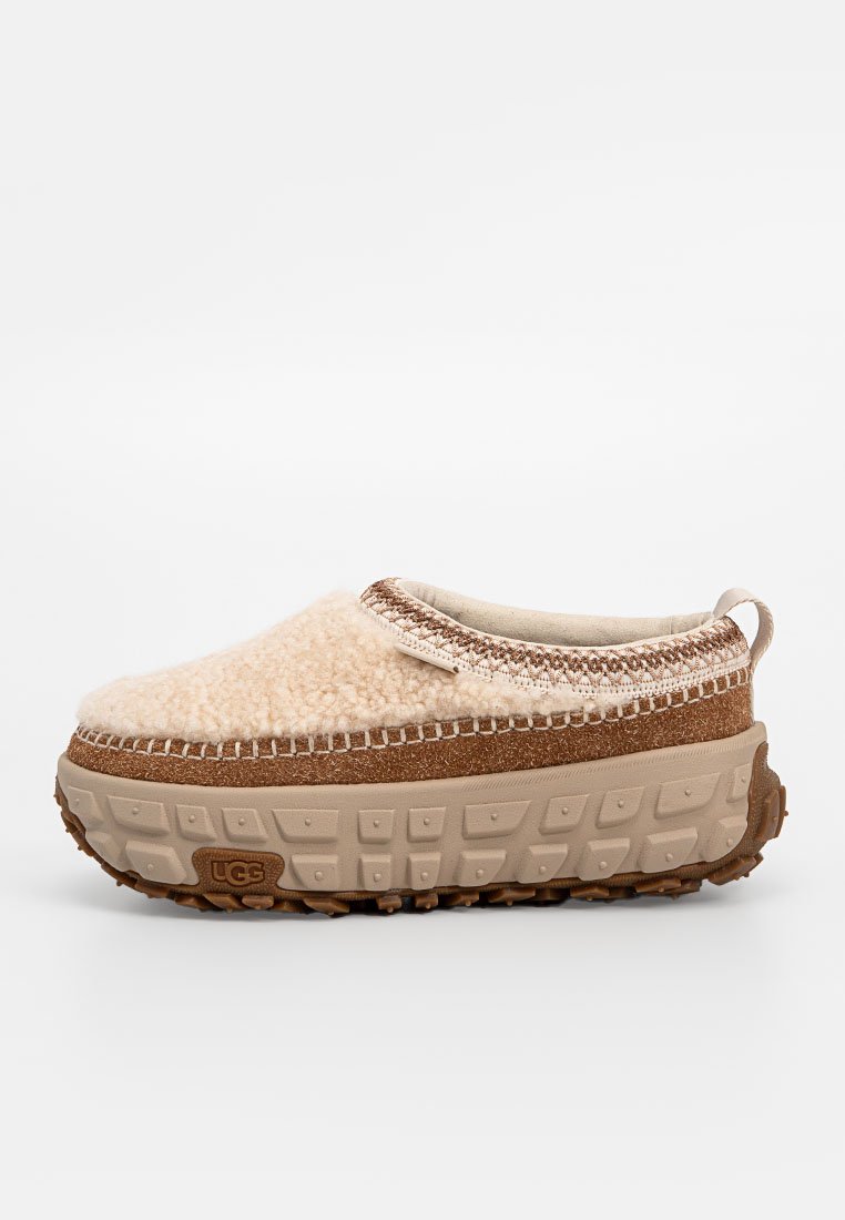 Zapato slip-on beige difuso con un upper texturizado, acentos marrones y una suela de goma gruesa con un diseño de dibujo.