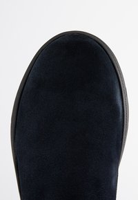 Scarpe in suede blu scuro con punta arrotondata, caratterizzate da una texture liscia e una suola in gomma nera a contrasto lungo il bordo.