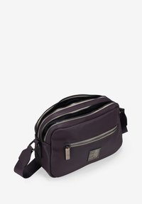 Bolso cruzado de nailon morado con múltiples compartimentos con cremallera, textura suave y un emblema de marca en el panel frontal.